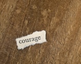 The word “courage” printed on torn paper placed on rustic wood.