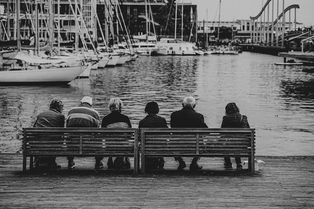 grayscale photo of people sitting on bench near body of water