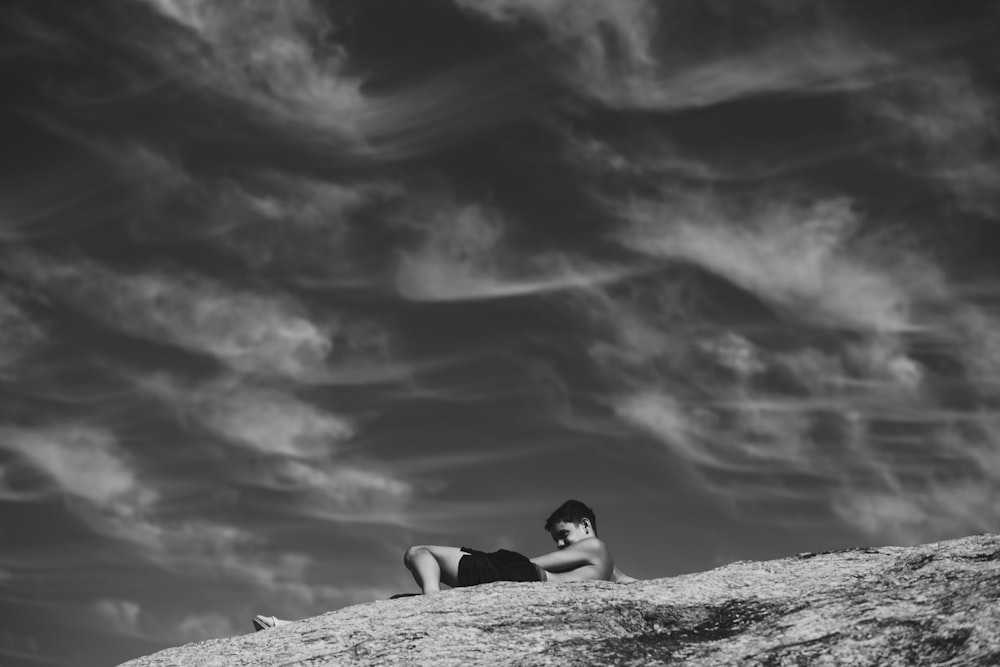 grayscale photo of woman lying on rock