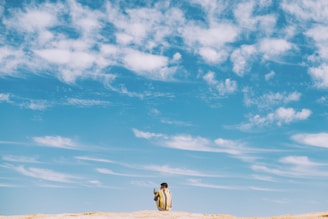 man and woman walking on brown sand under blue sky and white clouds during daytime