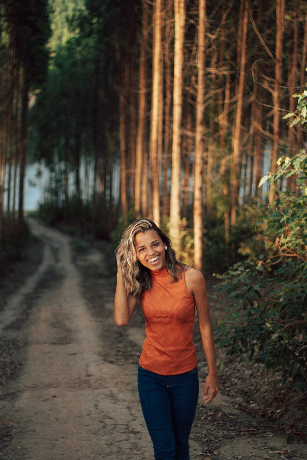 woman in orange tank top and red shorts standing on dirt road