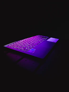 A sleek laptop keyboard illuminated with blue neon lights against a dark tech-themed background.