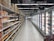An aisle in a supermarket with shelves on the left displaying a variety of packaged goods, including sauces and snacks. On the right, there is a long row of freezer units containing frozen products. The floor is tiled, and there is bright artificial lighting from overhead.