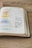 An open book lies on a wooden surface with handwritten notes and highlighted text in various colors. The pages display a mix of printed text and personal annotations made by someone studying or reflecting on the content.