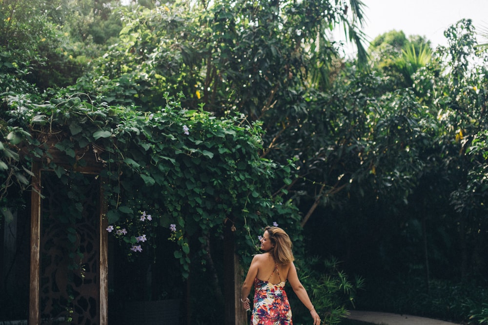 woman in blue and red floral dress standing near green trees during daytime