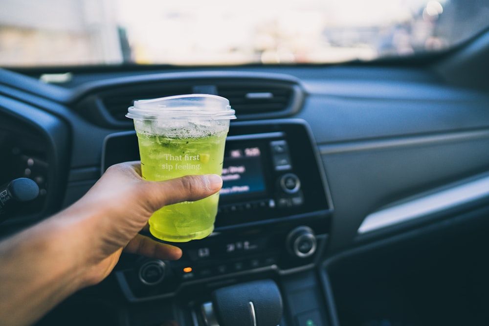 person holding clear plastic cup with yellow liquid inside