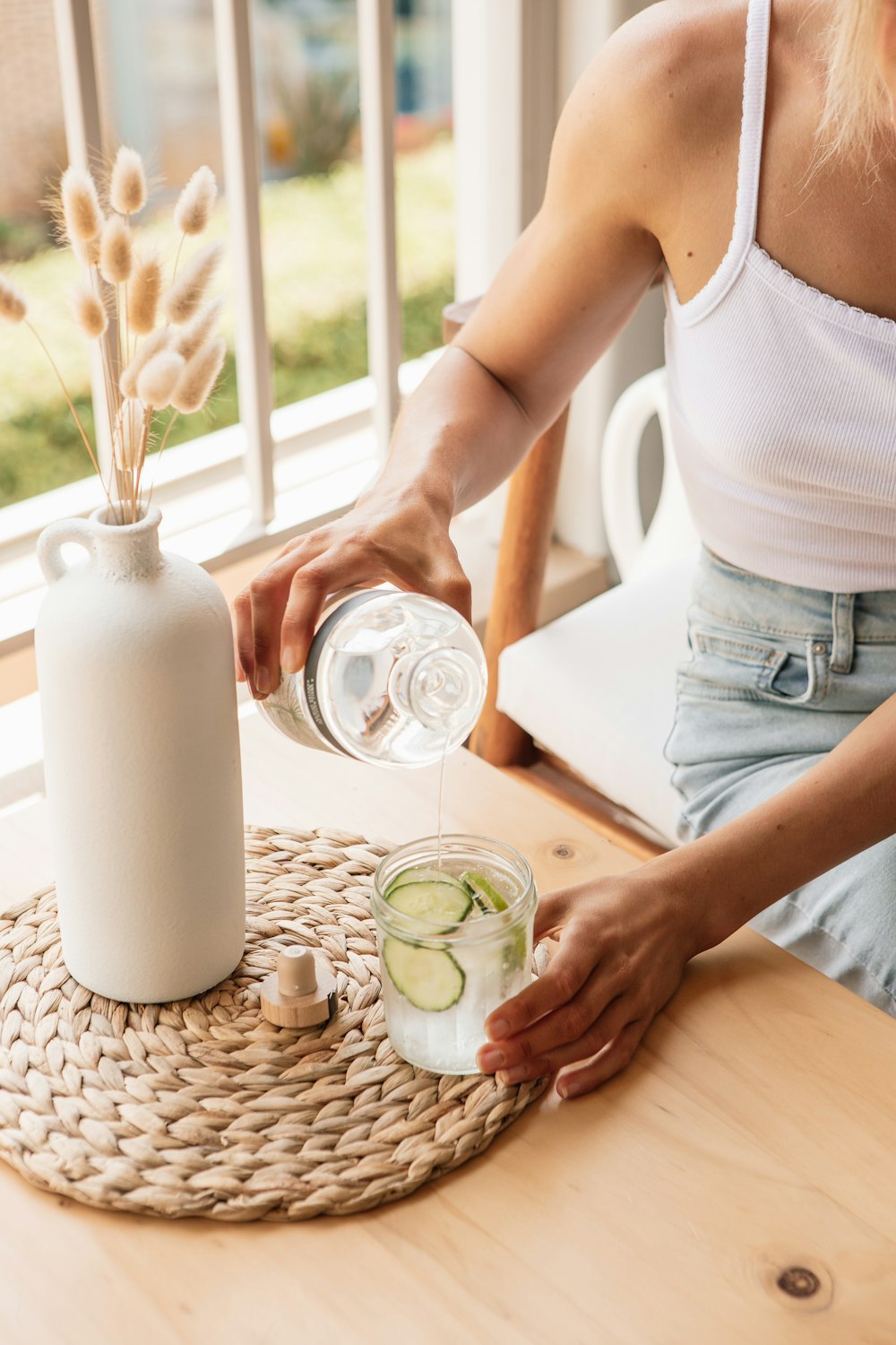 Frau in weißem Tanktop gießt Wasser auf klares Trinkglas
