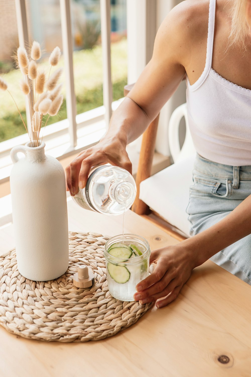 mulher na regata branca derramando água no vidro de beber transparente