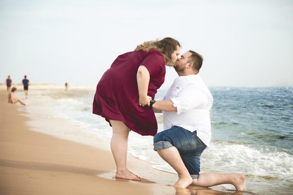 woman in white shirt carrying girl in red hoodie on beach during daytime