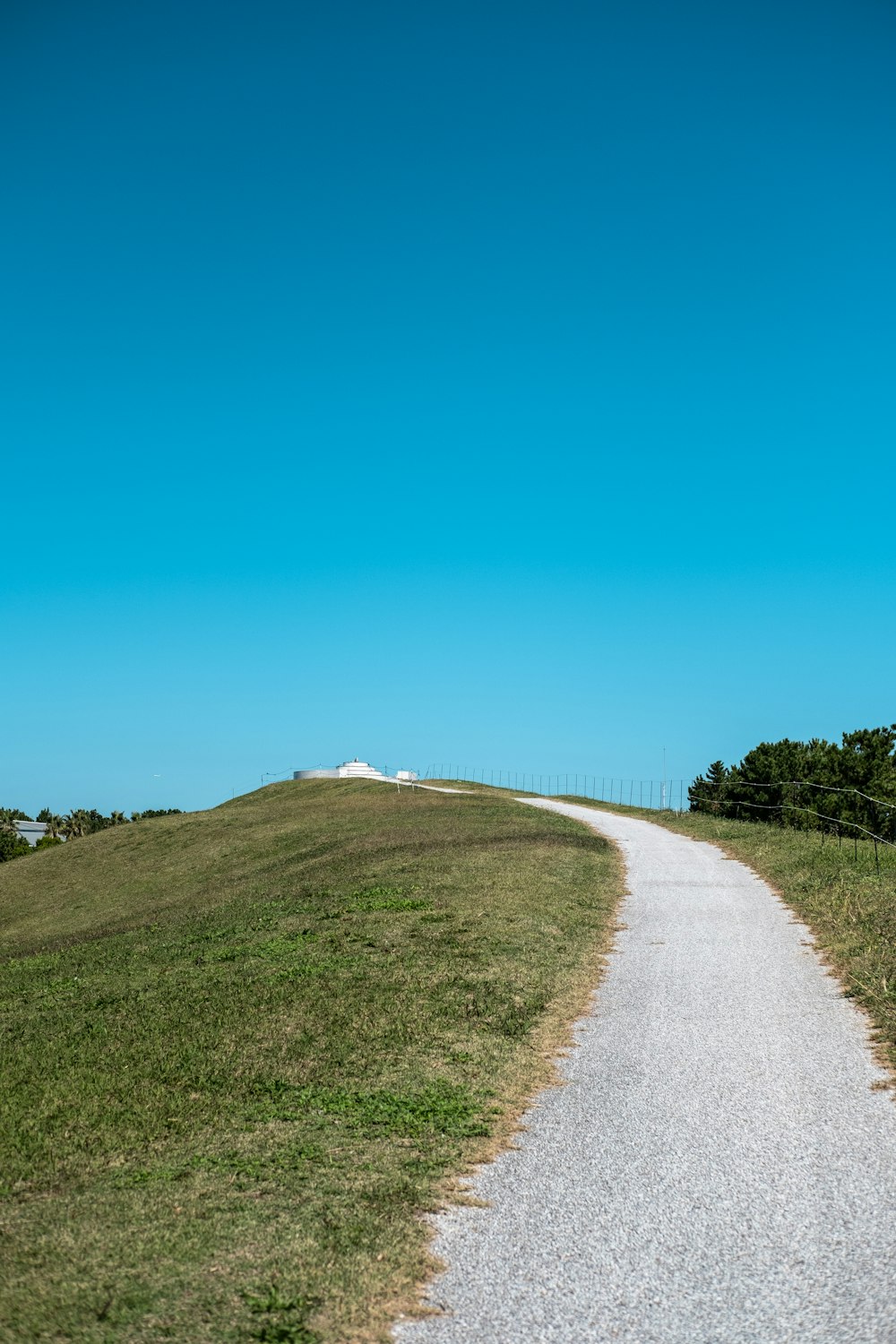 camino gris entre campo de hierba verde bajo cielo azul durante el día