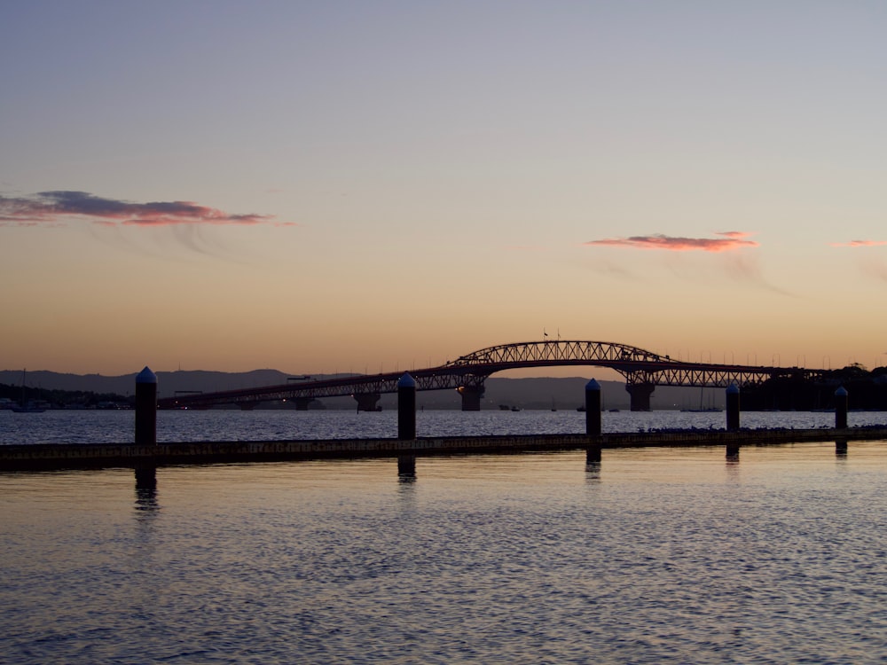 silhouette of bridge over body of water during sunset