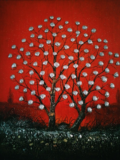 A stylized tree with branches covered in metallic, disc-like objects set against a rich red background. The ground is textured with dark, swirling patterns and small stones.
