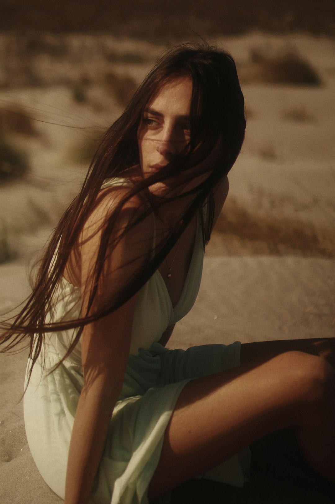 woman in white tank top and green shorts sitting on sand during daytime