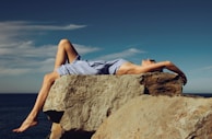 woman in blue denim shorts lying on brown rock during daytime