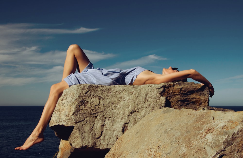 Mujer en pantalones cortos de mezclilla azules acostada en una roca marrón durante el día