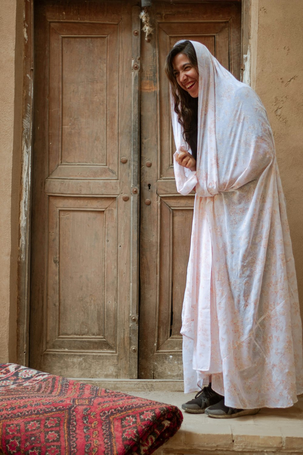 茶色の木のドアの横に立つ白いローブの女性