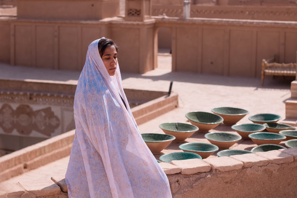 Mujer con hiyab blanco de pie cerca de una palangana de plástico redonda verde
