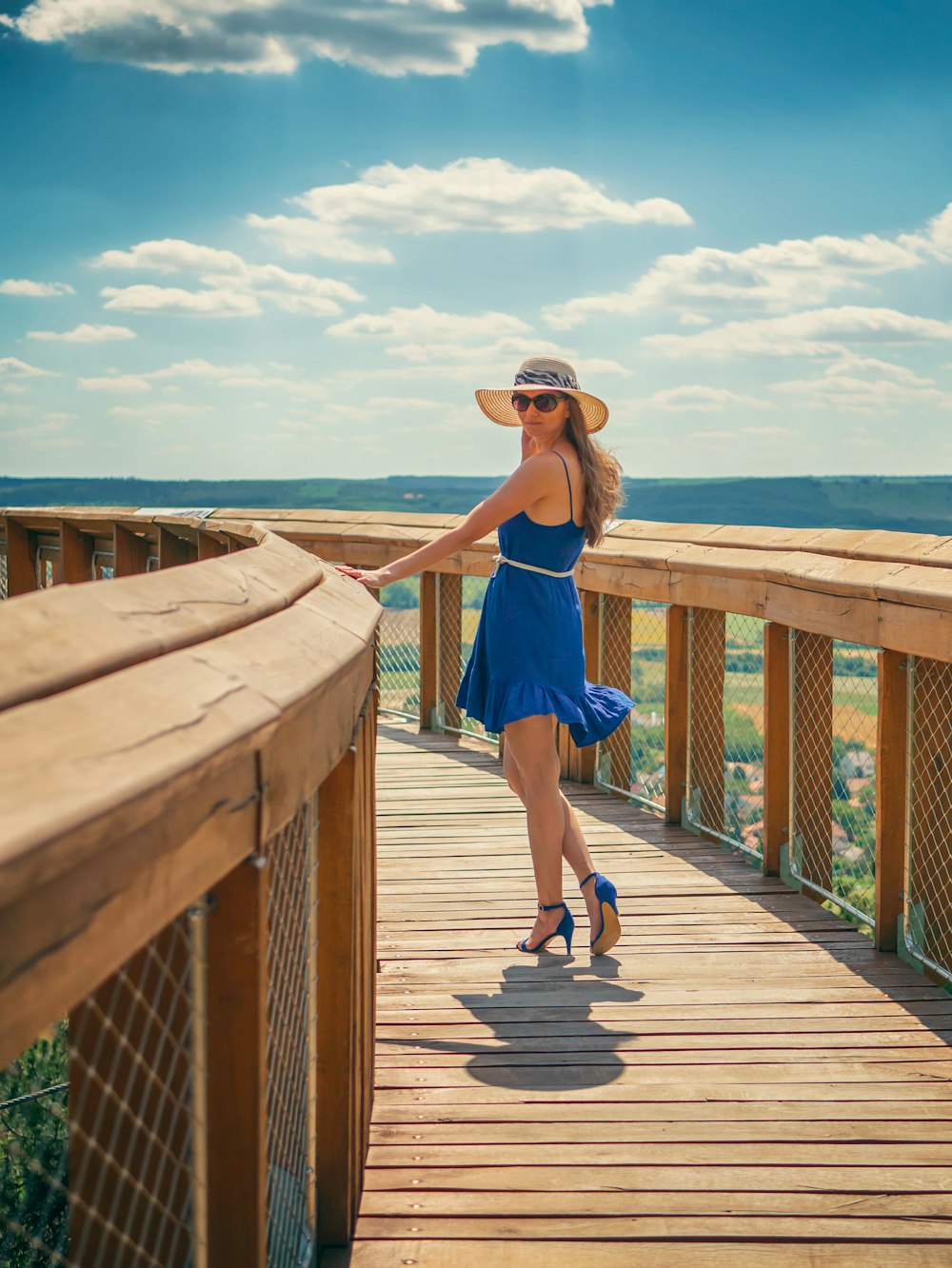 woman in blue tank top and blue shorts standing on brown wooden dock during daytime
