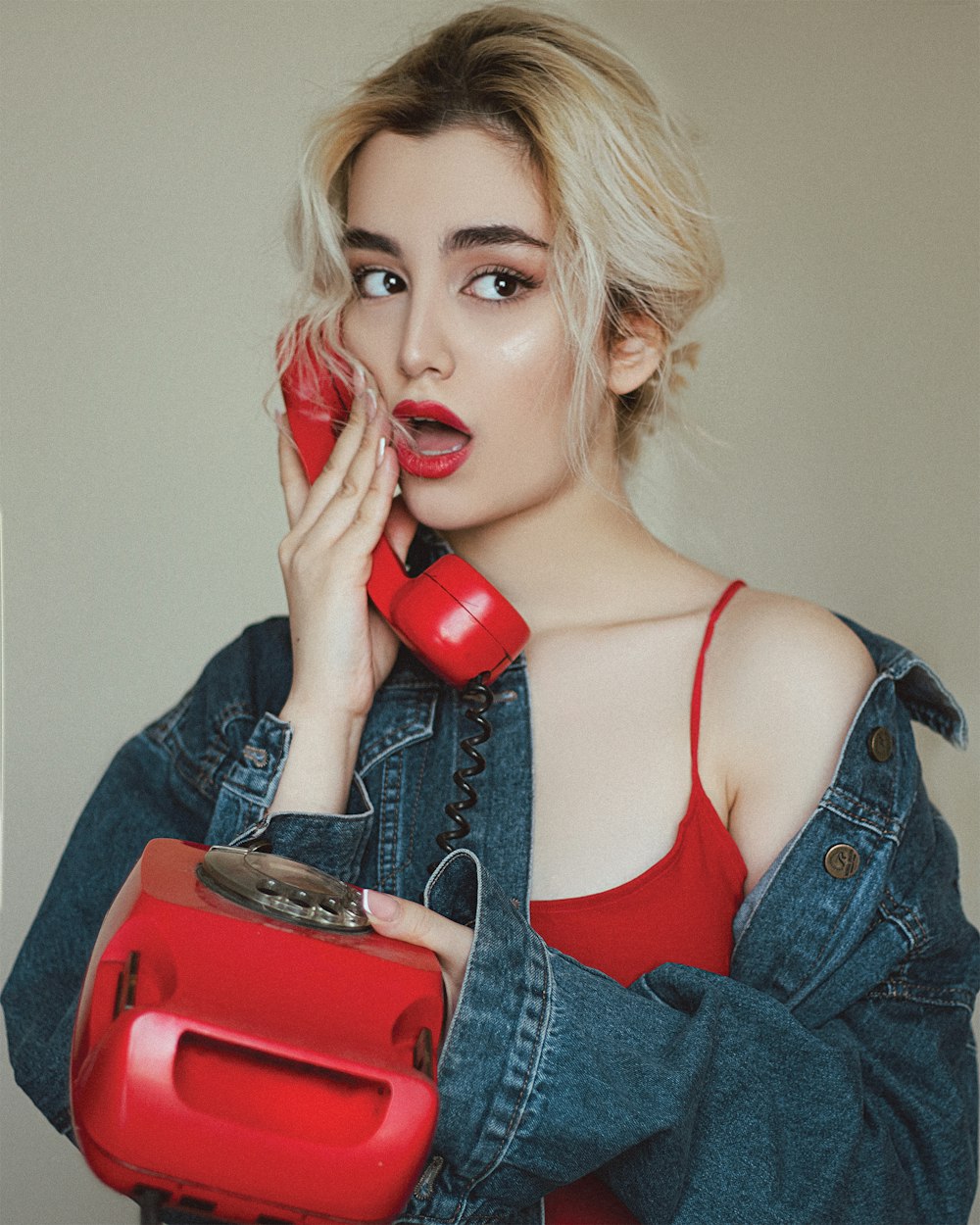 赤い電話を持つ青いデニムジャケットの女性