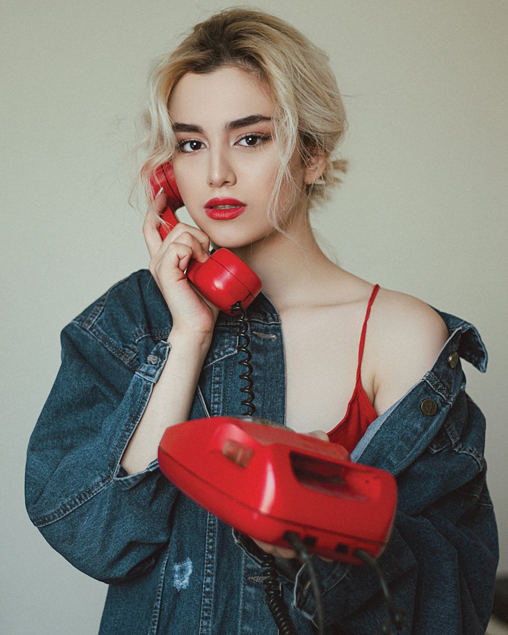 woman in blue denim jacket holding red telephone