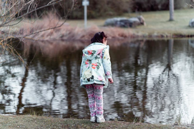 woman in white pink and green floral dress standing on brown grass field near lake during