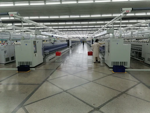 A bright factory floor showing polyester fiber machines in operation with workers monitoring the process.