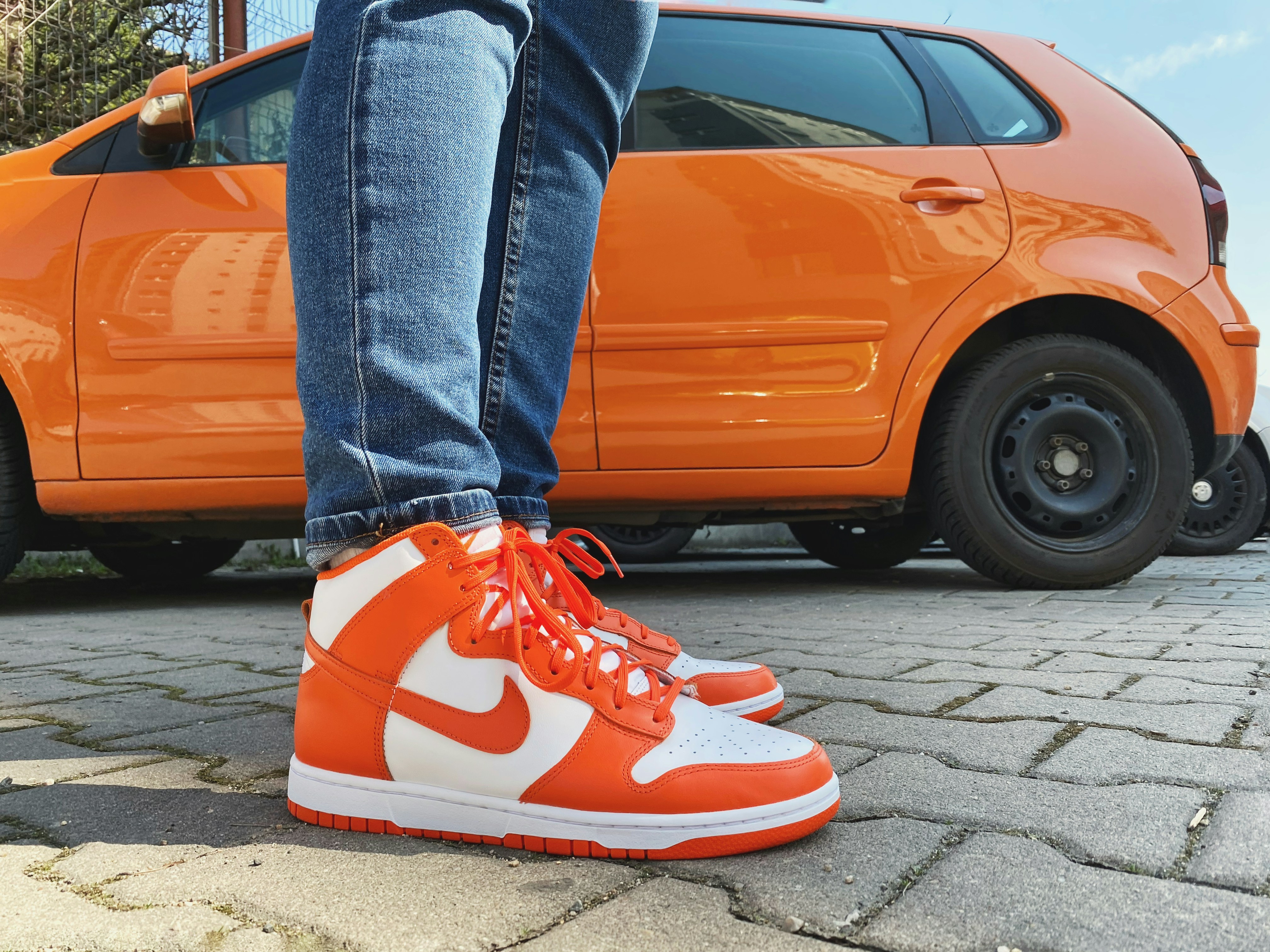 person in blue denim jeans and red nike sneakers standing beside orange car