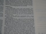Close-up view of a book page with text in a structured format, resembling a biblical or literary passage. The text includes a narrative involving characters and dialogue. The page layout includes a header and numbered lines, suggesting a divided section of content.