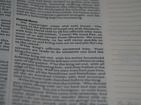 Close-up view of a book page with text in a structured format, resembling a biblical or literary passage. The text includes a narrative involving characters and dialogue. The page layout includes a header and numbered lines, suggesting a divided section of content.