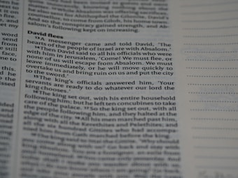 Close-up view of a book page with text in a structured format, resembling a biblical or literary passage. The text includes a narrative involving characters and dialogue. The page layout includes a header and numbered lines, suggesting a divided section of content.