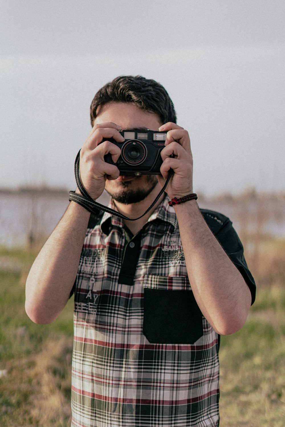 man in red white and black plaid button up shirt holding black dslr camera