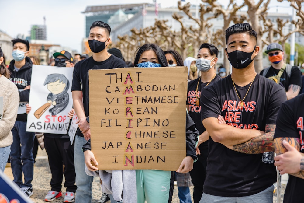 man in black crew neck t-shirt holding brown wooden signage