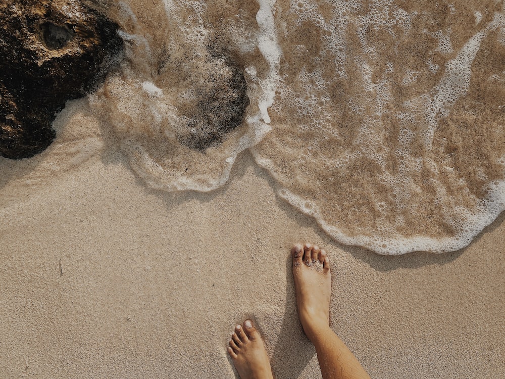 pessoa em pé na areia marrom perto do corpo de água durante o dia