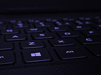 A close-up view of a black keyboard, focusing on the Windows and Alt keys in the bottom row. The keys are slightly illuminated in a dark environment, and the letters are clearly visible.