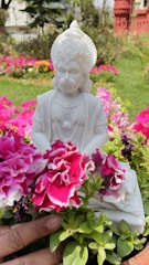 Statue of Shakira in Barranquilla surrounded by colorful flowers and blue sky.