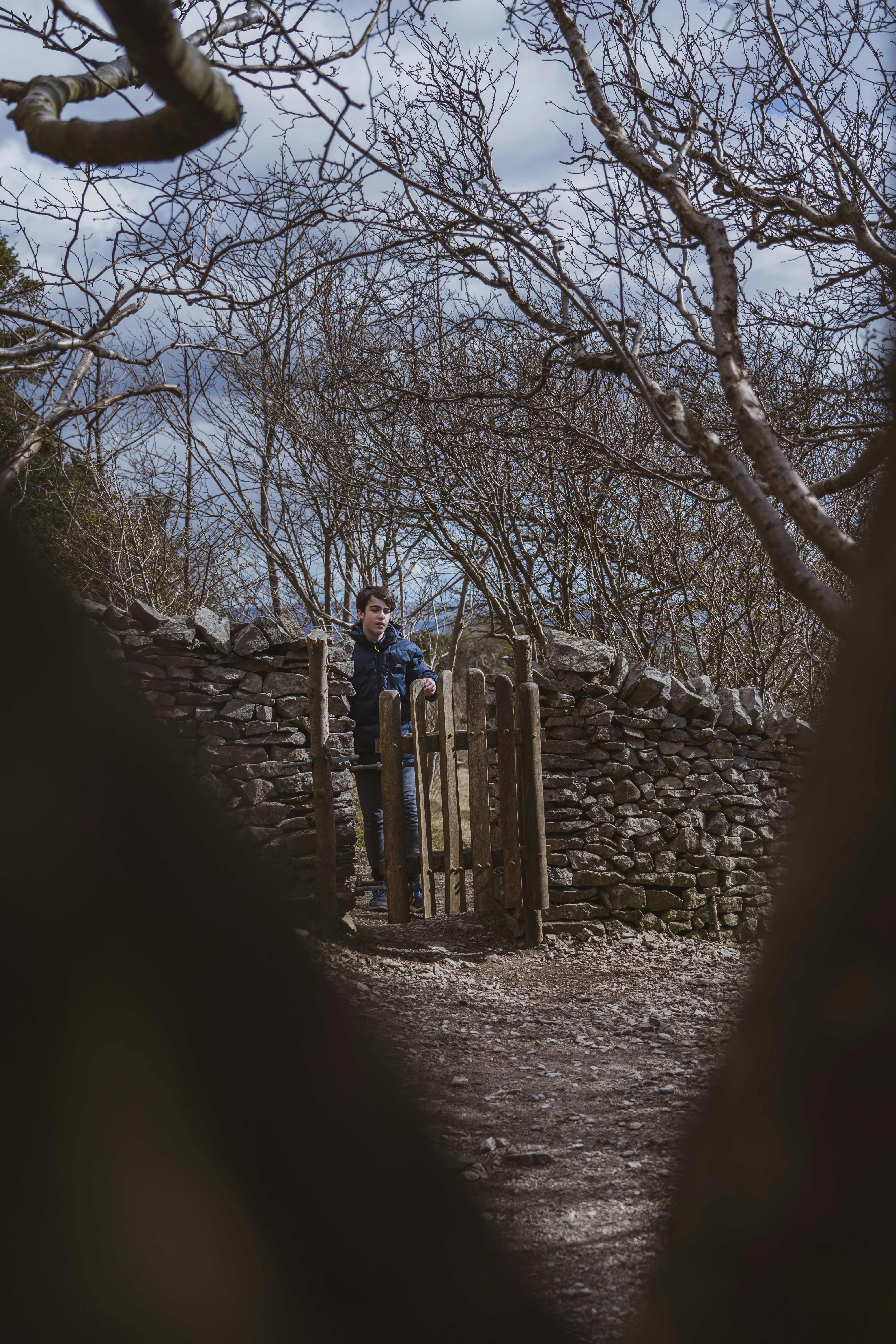 man in blue jacket standing on brown wooden fence during daytime