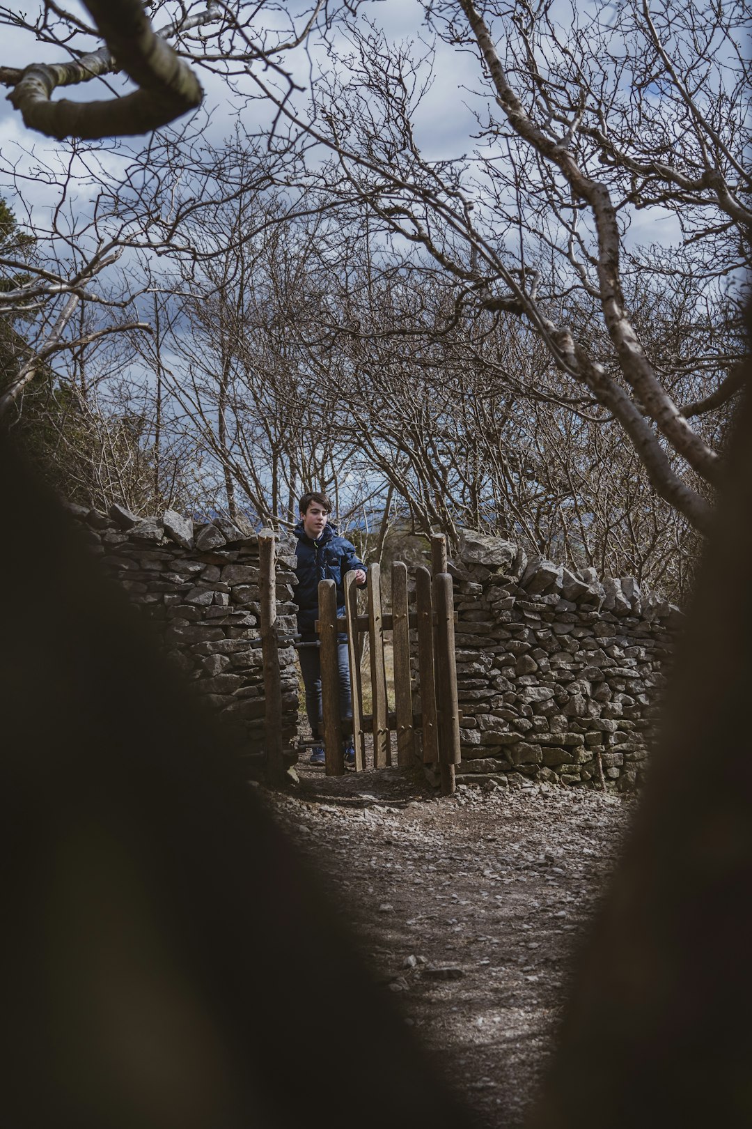 man in blue jacket standing on brown wooden fence during daytime