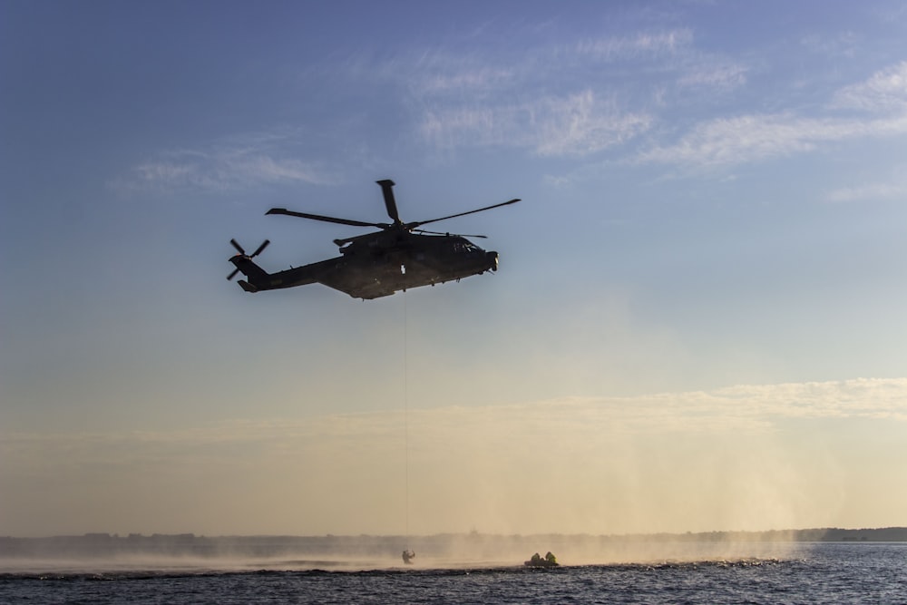 black helicopter flying over the sea during daytime