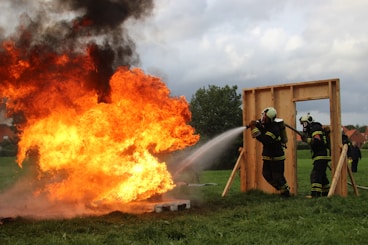man in black jacket and black pants standing near burning wood during daytime