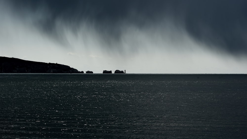 silhouette of rock formation on sea under white clouds