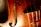 Close-up view of a violin showcasing its warm wooden texture with visible wood grain. The image captures part of the violin's body, F-hole, strings, and a label inside which reads 'GRANDJON MIRECOURT'. The lighting highlights the instrument's glossy finish and fine craftsmanship.