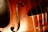 Close-up view of a violin showcasing its warm wooden texture with visible wood grain. The image captures part of the violin's body, F-hole, strings, and a label inside which reads 'GRANDJON MIRECOURT'. The lighting highlights the instrument's glossy finish and fine craftsmanship.