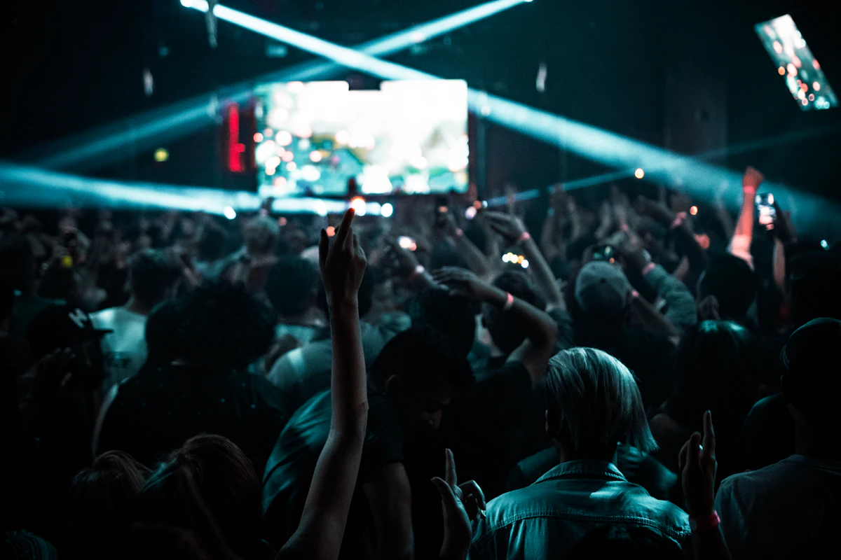 Crowd from behind raising hands toward a stage with teal lights and a screen