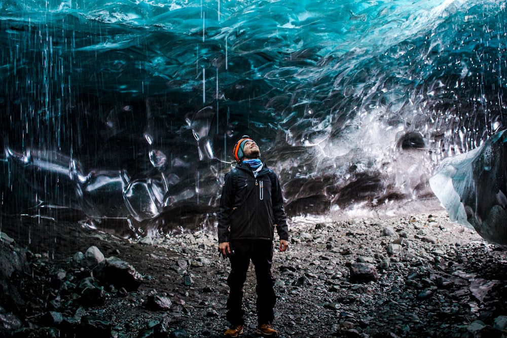 man in black jacket and black pants standing on rocky ground