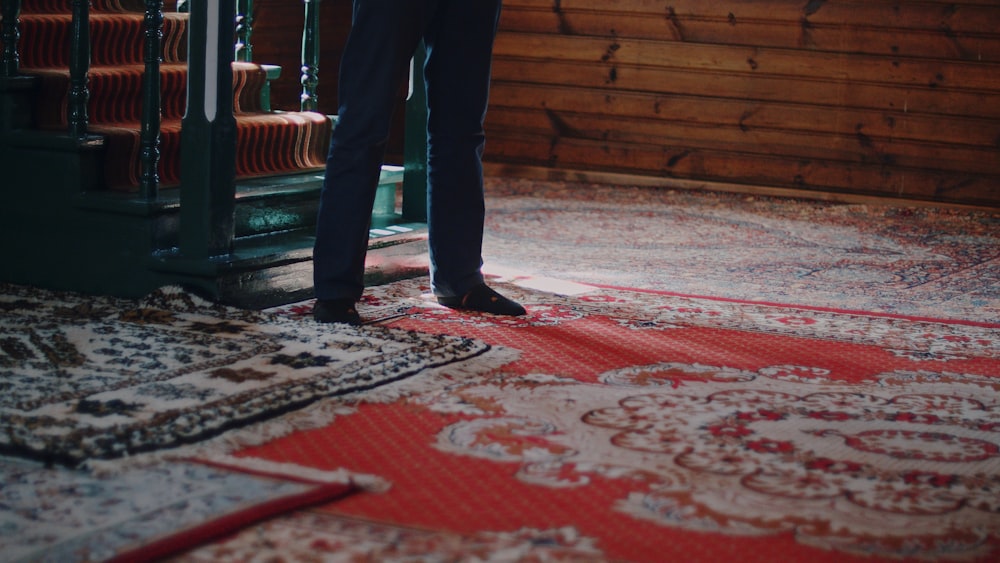 person in black pants standing on red and white floral area rug