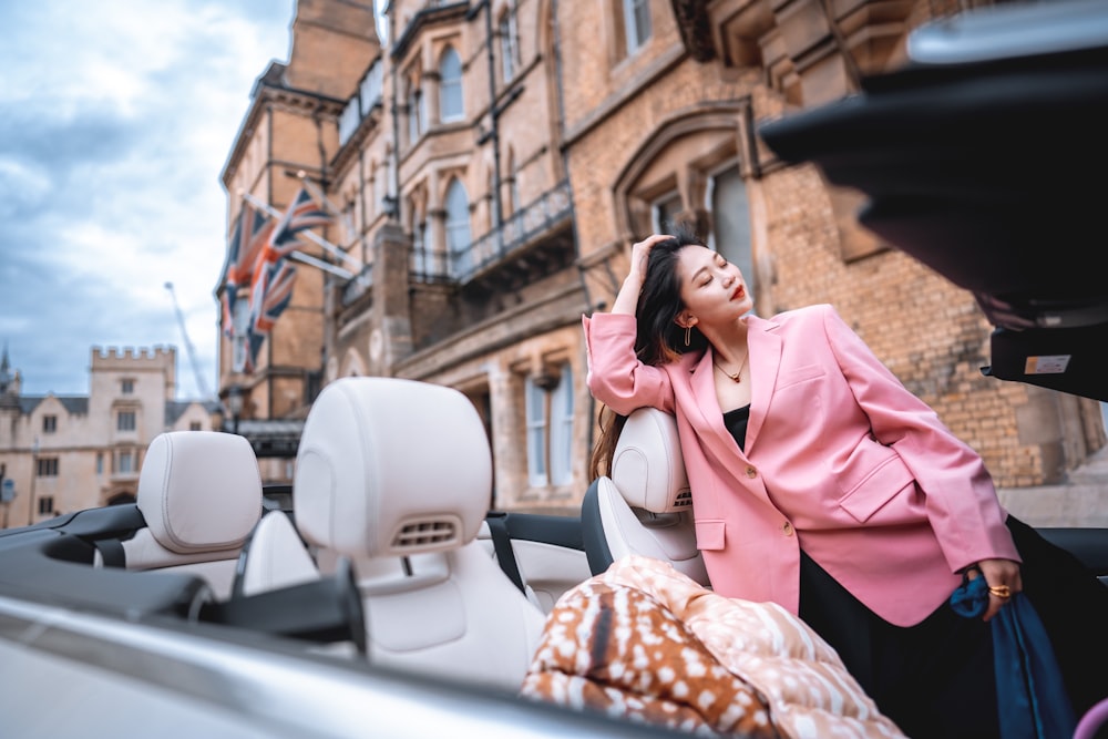 woman in pink coat and white knit cap sitting on white car