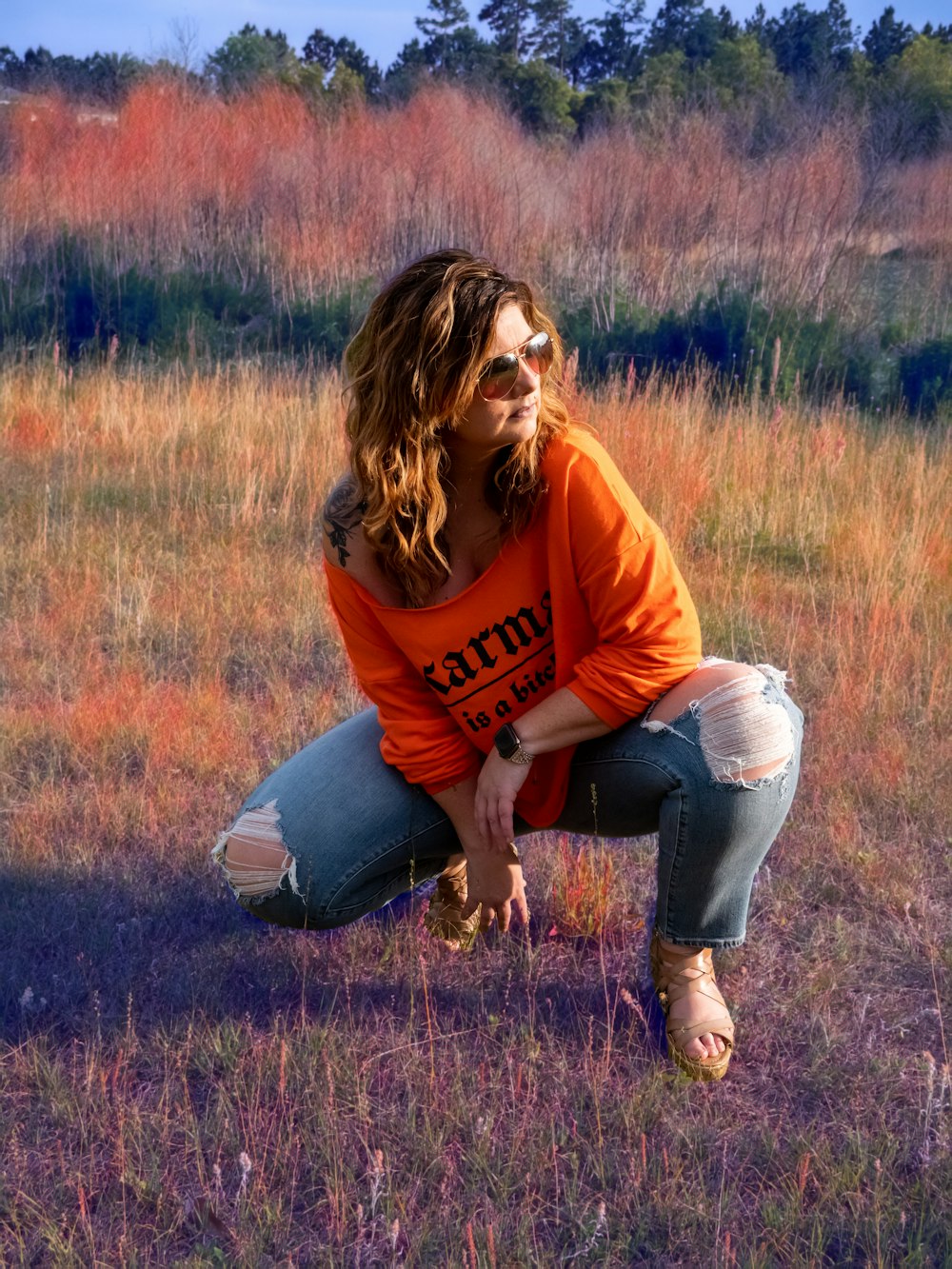 woman in orange long sleeve shirt and blue denim jeans sitting on brown grass field during