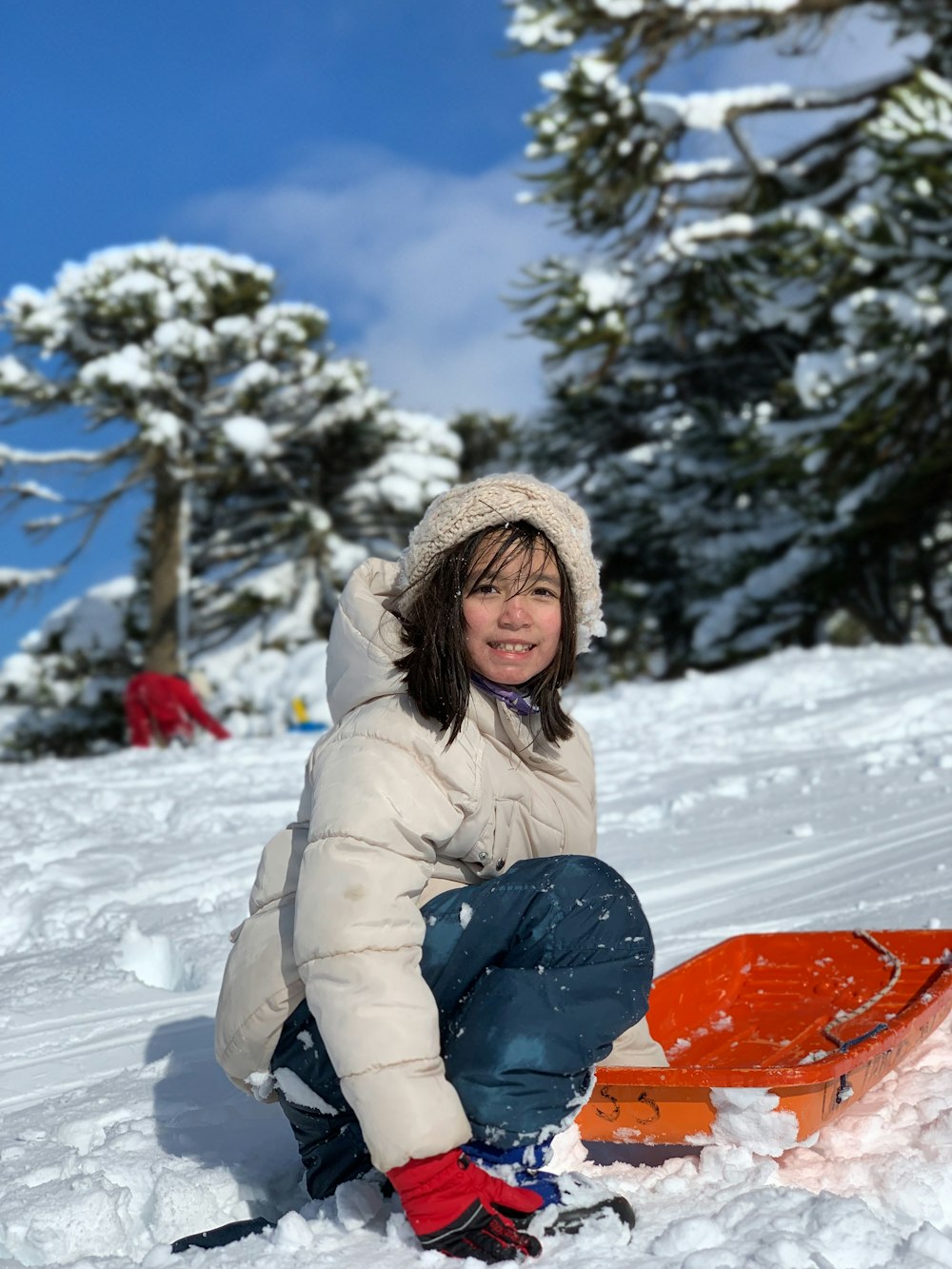 Frau in grauer Jacke und blauer Hose sitzt tagsüber auf schneebedecktem Boden