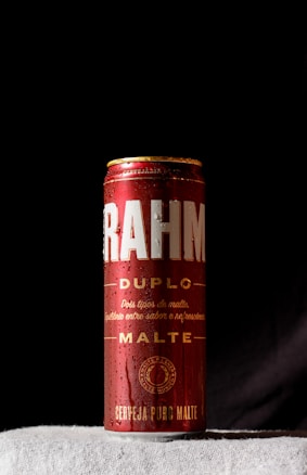 A single can of Brahma Duplo Malte beer prominently displayed against a dark background. The can is red with white and gold text, with droplets of condensation visible, suggesting it is cold.