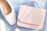 Close-up of a chic beige handbag resting on a soft rose-pink fabric.